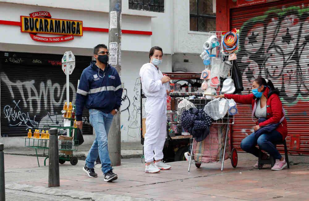 Algunos vendedores informales ubican su puesto de venta frente a los locales que permanecen cerrados por orden de la alcaldía. En este caso la mujer usa un traje antifluidos y el tapabocas para atender a su clientela. Claudia López reiteró, este jueves, que no autorizará la reapertura de sectores distintos a la manufactura, la construcción y el comercio de bienes esenciales. Foto: Guillermo Torres / SEMANA.
