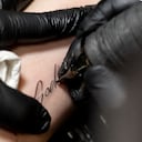 El tatuador Silas Becks coloca un parche protector sobre un tatuaje que dice "Dios" en el brazo de un joven el 15 de abril de 2023 en Viena, Austria. (Photo by JOE KLAMAR / AFP)