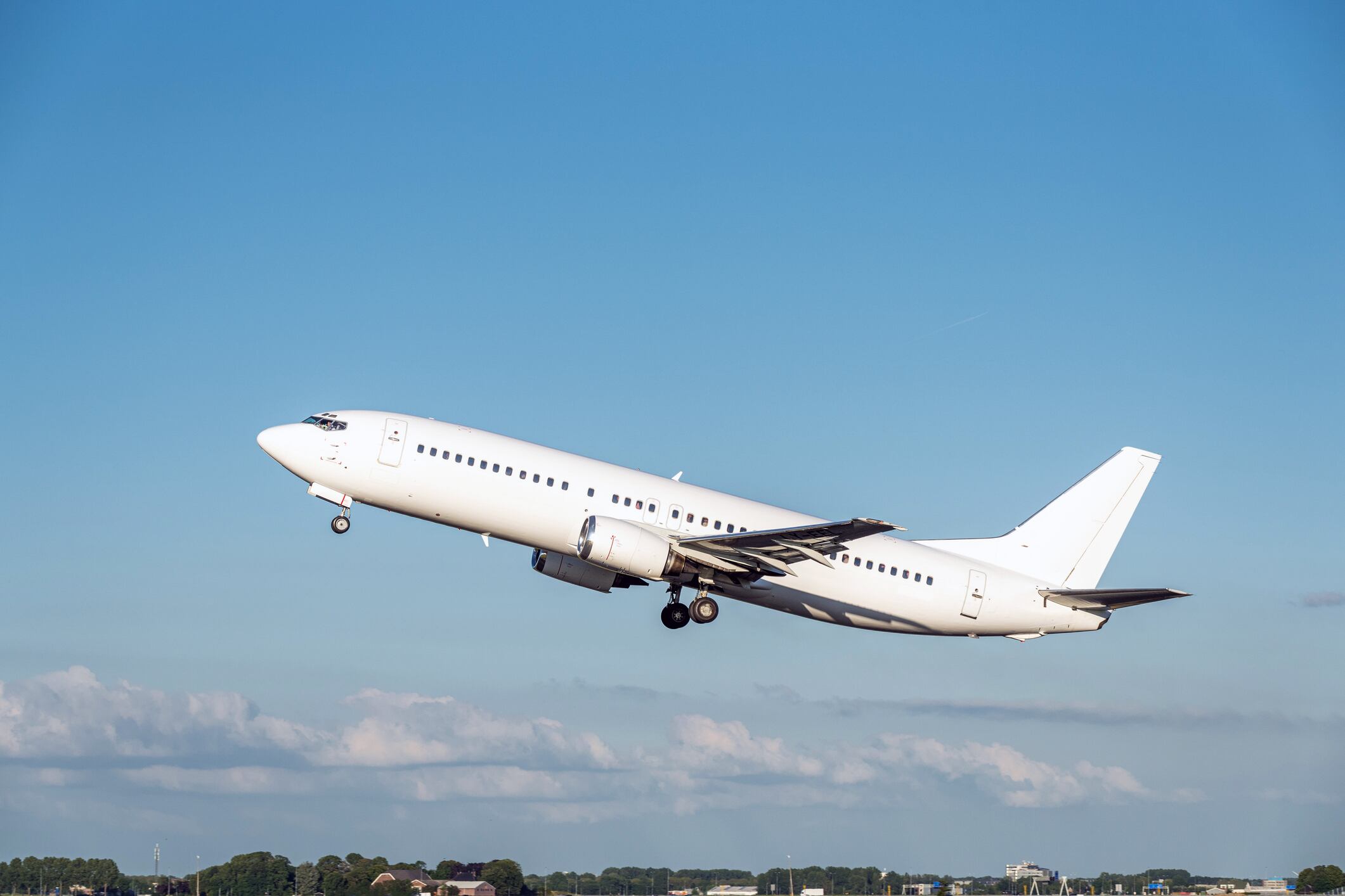 This is a picture of an all white white commercial airplane taking off from an airport on a warm, sunny day.