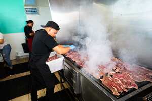 Joven chef colocando cortes de carne en la parrilla en un restaurante.