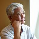 Retrato de un hombre mayor asiático triste sentado junto a la ventana con la mano en la barbilla.