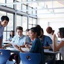 Teacher assisting group of students in classroom, looking at tablet