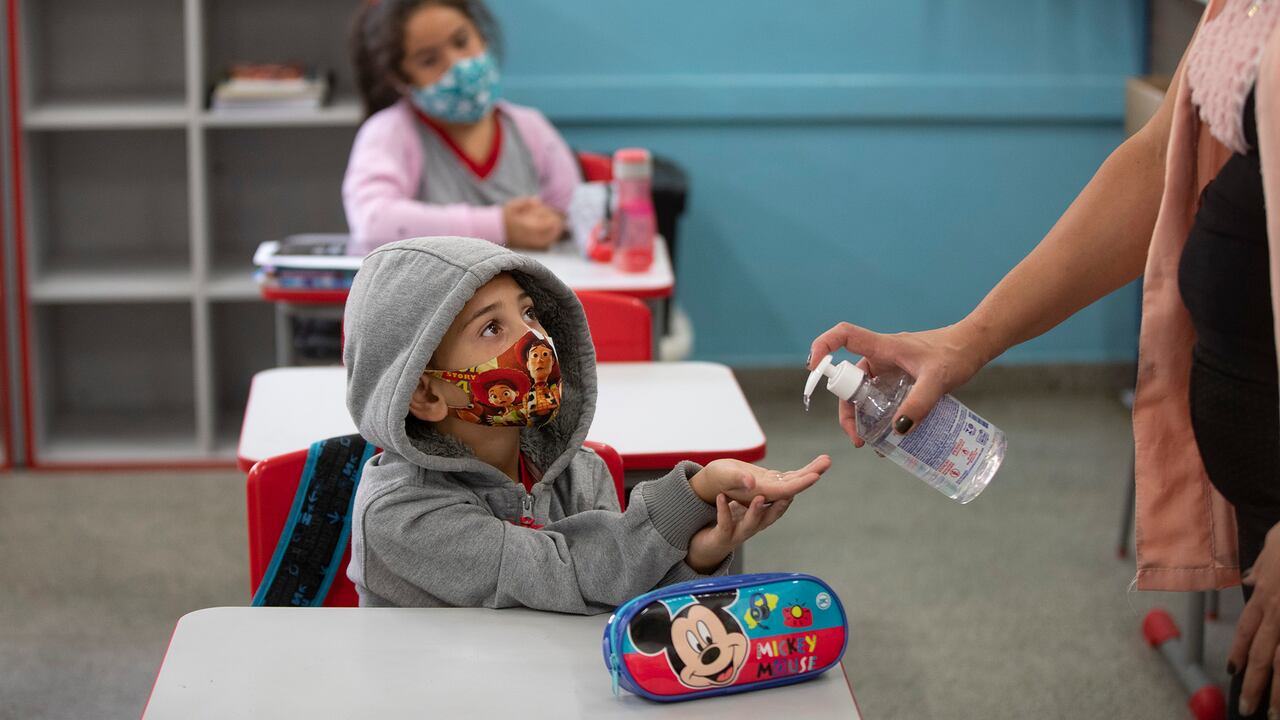 Un estudiante recibe un chorro de gel antibacteriano de su maestra el primer día de regreso a clases presenciales en medio de la pandemia de COVID-19 en la escuela pública Raúl Antonio Fragoso en Sao Paulo, Brasil, el lunes 8 de febrero de 2021. El gobierno del estado de Sao Paulo ha permitido que las escuelas reanuden las clases con hasta un 35% de sus estudiantes. (Foto AP / Andre Penner)