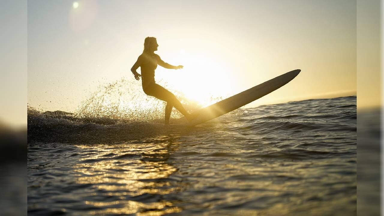 Una mujer navega en una tabla larga mientras se pone el sol en un día caluroso el jueves 13 de julio de 2023 en Encinitas, California.