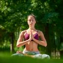 Full length shot of a young woman sitting in lotus pose and practicing yoga in the city park.