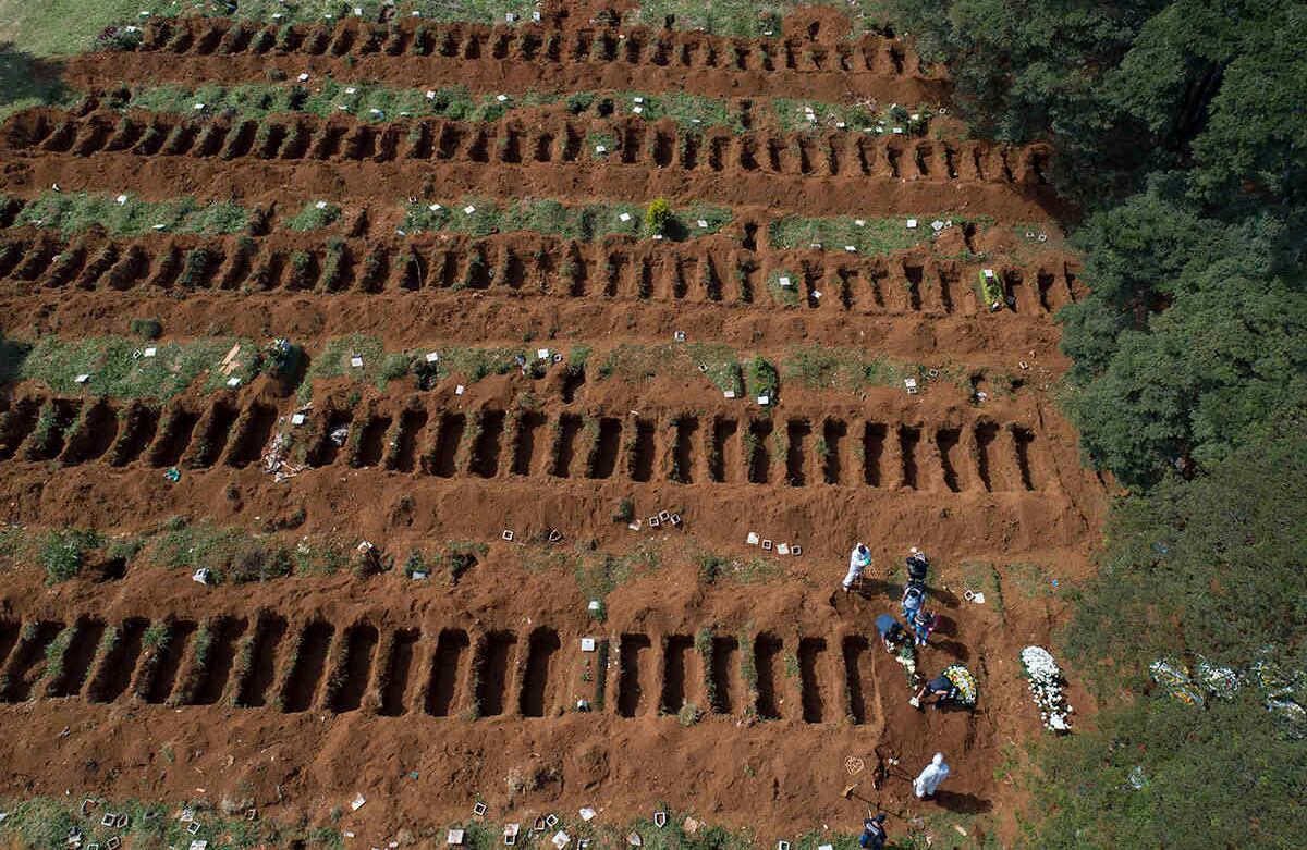 Operarios con trajes de protección entierran a una persona junto a una fila de tumbas recién excavadas, en el cementerio de Vila Formosa, en Sao Paulo, Brasil. Según sus responsables, Vila Formosa, el camposanto más grande de Latinoamérica, registró un incremento del 30% en el número de entierros durante la crisis del coronavirus. Foto: Andre Penner/ AP. 