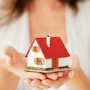 Close-up of woman's hands holding a small model house. Horizontal shot. Isolated on white.