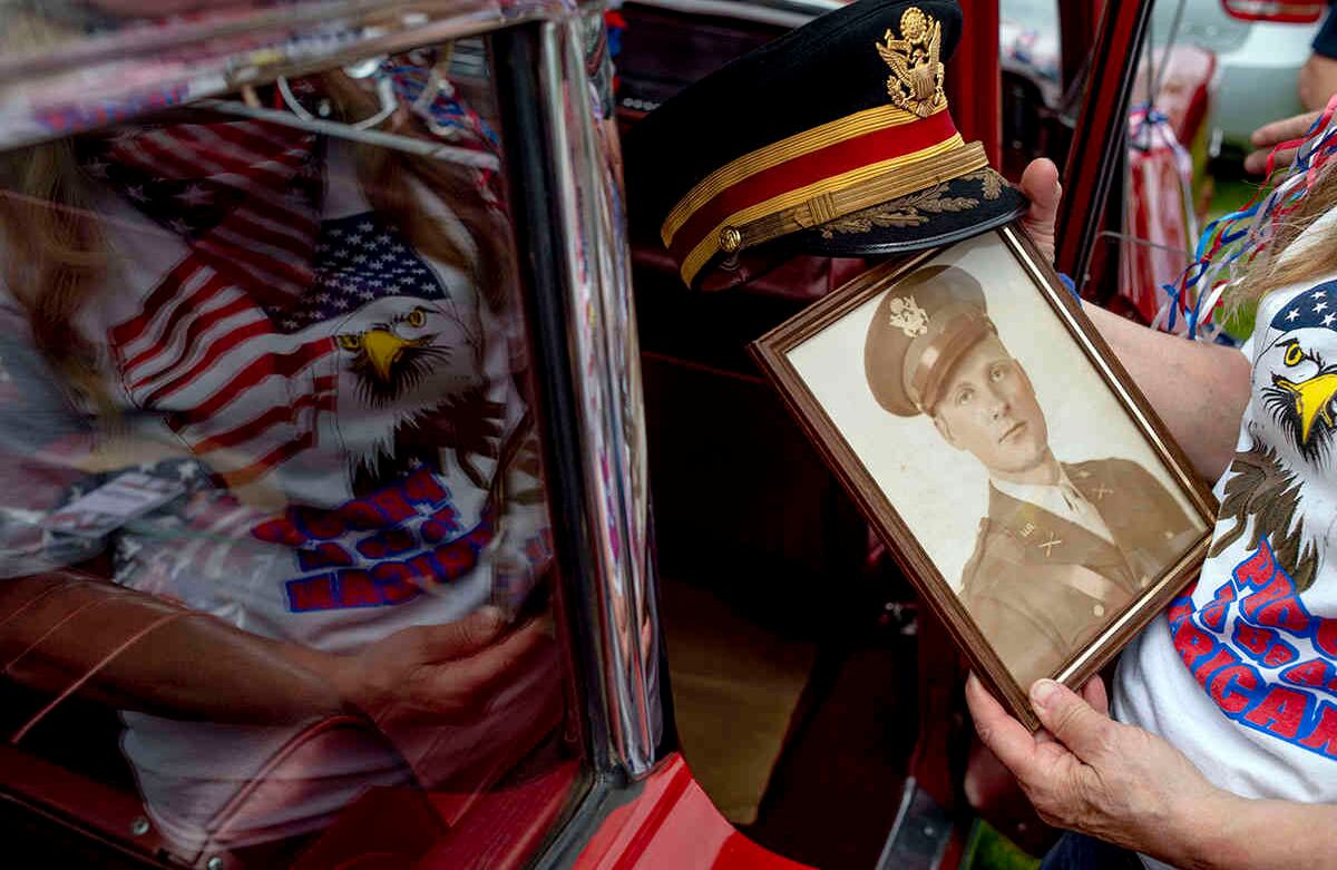 Cindy Gabriel muestra una fotografía de su difunto padre, el teniente coronel James W. Miller, quien sirvió en la Segunda Guerra Mundial y la Guerra de Corea, durante un desfile y ceremonia del Día de los Caídos, observando el distanciamiento social durante el brote de coronavirus, el lunes 25 de mayo de 2020, en el Parque Anrook en Lapeer, Mich. (Jake May / The Flint Journal a través de AP)