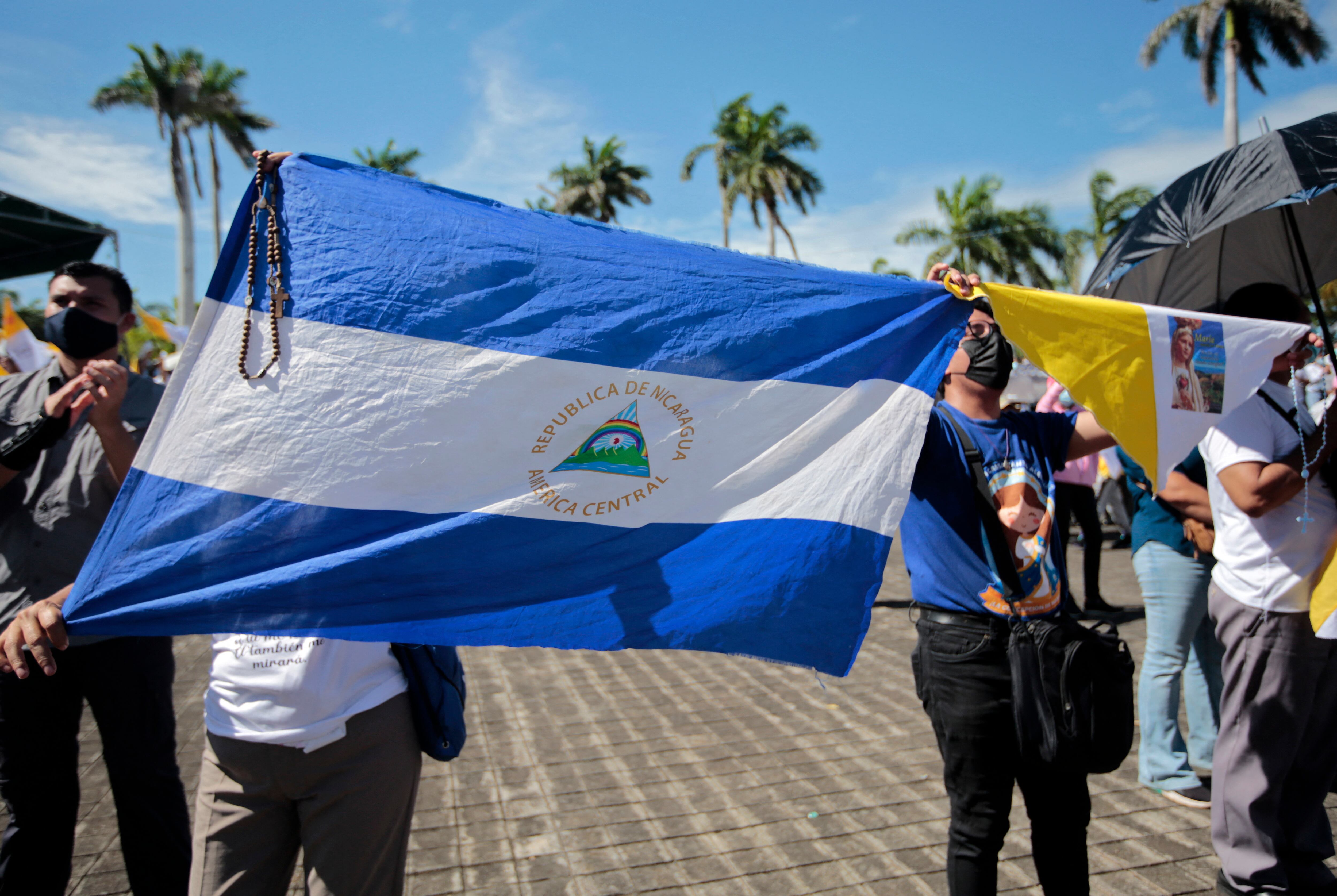 Una mujer sostiene una bandera nacional nicaragüense durante una procesión de la Virgen de Fátima dentro de los terrenos de la Catedral Metropolitana de Managua el 13 de agosto de 2022. - La policía de Nicaragua ha prohibido una procesión prevista por la Iglesia Católica en la capital "por razones de seguridad interna", dijo el viernes la arquidiócesis de Managua. La medida se produce cuando un destacado obispo católico permanece bloqueado dentro de su residencia por la policía. A pesar de la prohibición de la procesión del sábado, la arquidiócesis pidió a los fieles que se dirigieran a la catedral de la capital para "orar por la iglesia nicaragüense". (Foto por Oswaldo RIVAS / AFP)