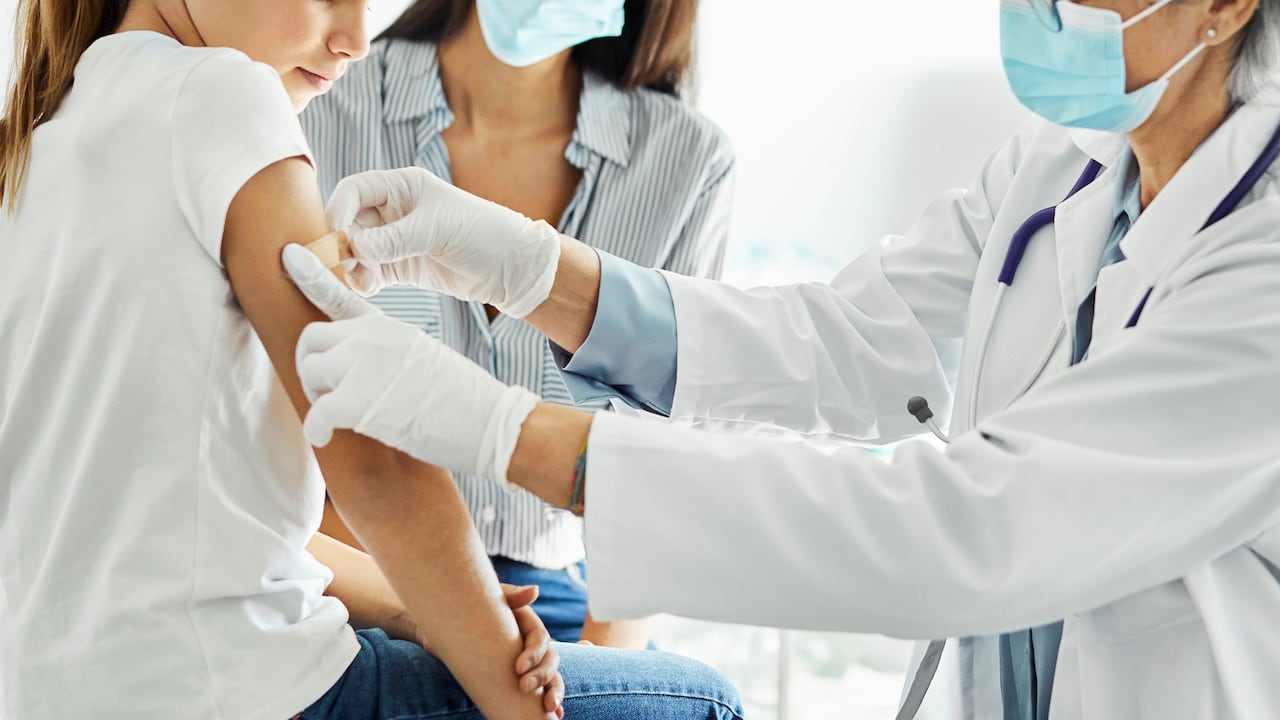 Niña recibiendo una vacuna de COVID-19 y mirando su brazo.