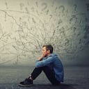 Un adolescente molesto y cansado sentado en el suelo mantiene la mano en la mejilla mirando pensativo y sin esperanza. El estudiante estresado siente incomodidad emocional, ansiedad y problemas de salud mental.