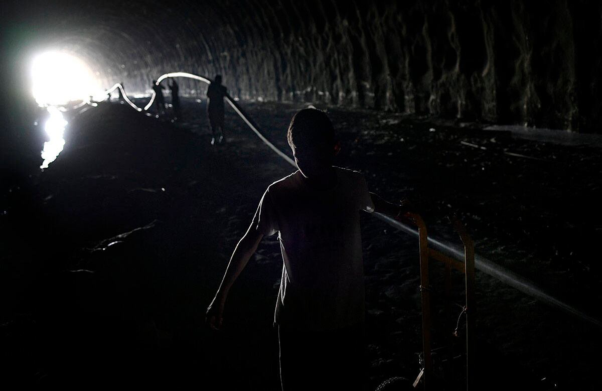 Un niño ayuda a conectar la tubería de agua dentro de un túnel de carretera abandonado. Al fondo se ve a más personas completando la labor para sacar el líquido vital. Foto: Matias Delacroix / AP