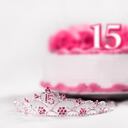 A tiara worn by a girl celebrating her 15th birthday is shot in front of a birthday cake. The focal point is on the tiara.