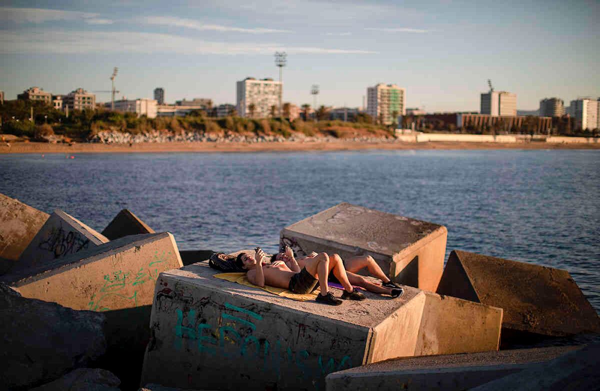 Dos hombres toman el sol frente al mar en Barcelona, España, el miércoles 20 de mayo de 2020. Barcelona permitió el miércoles que las personas caminen por sus playas por primera vez desde el inicio del bloqueo del coronavirus hace más de dos meses. (Foto AP / Emilio Morenatti)