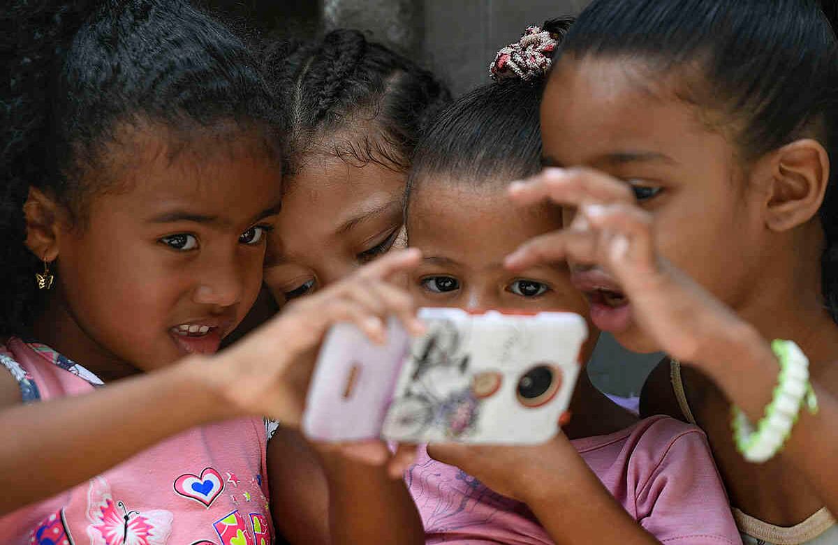 Niños venezolanos juegan con un teléfono inteligente durante la fiesta de San Juan Bautista en San Agustín, barrio de Caracas el 24 de junio. La fiesta tradicional es celebrada con una procesión por el barrio con la estatua de San Juan el Bautista, pero la cuarentena redujo la fiesta a una reunión de vecinos. Foto: Matias Delacroix/ AP