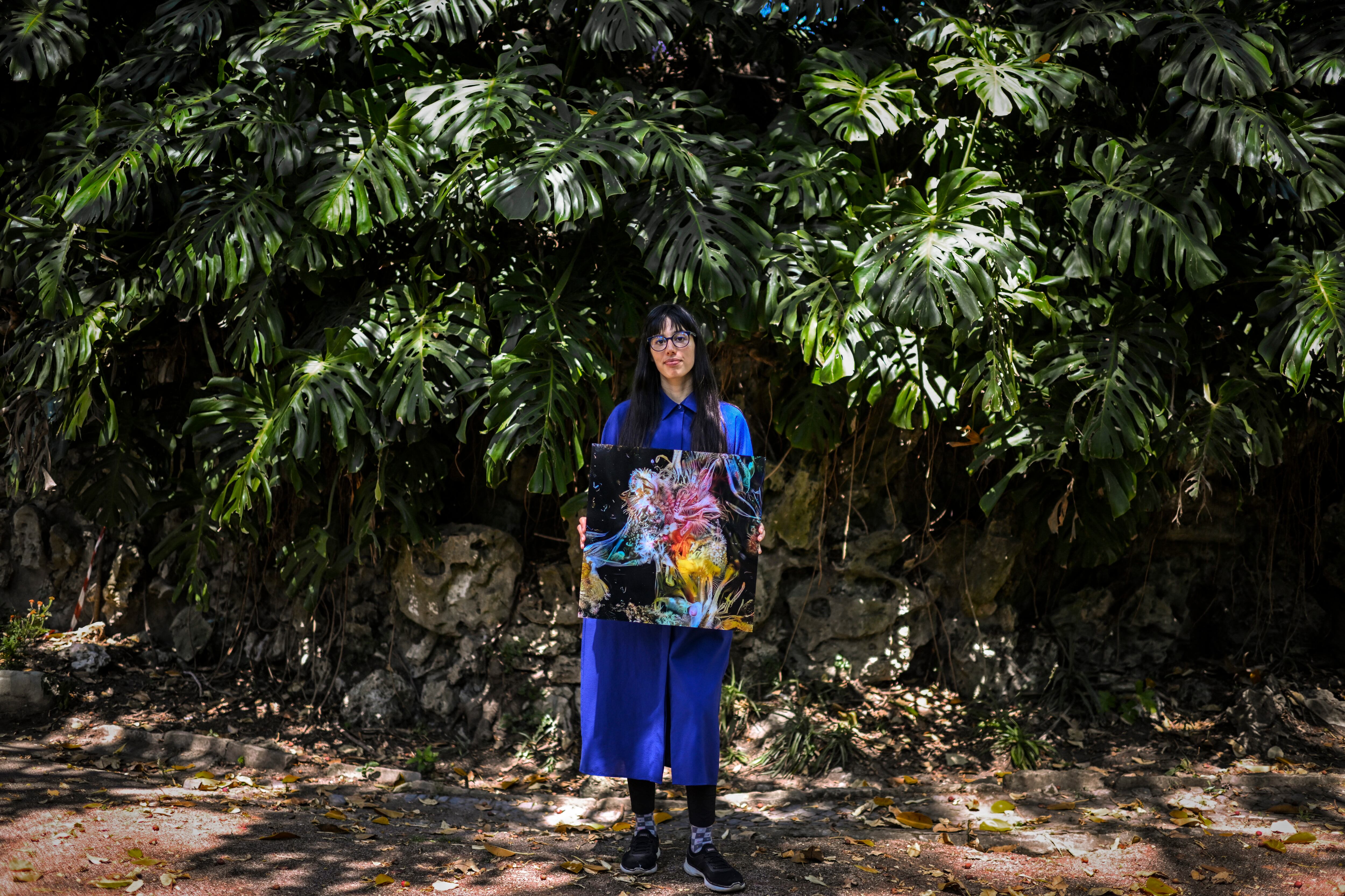 La artista argentina Sofia Crespo sostiene una de sus obras mientras posa para una foto en el jardín Estrela en Lisboa el 8 de junio de 2022. - La artista argentina Sofia Crespo, que crea sus obras con la ayuda de inteligencia artificial, es parte del " movimiento de arte generativo", donde los humanos crean reglas para las computadoras que luego usan algoritmos para generar nuevas formas, ideas y patrones. (Foto por PATRICIA DE MELO MOREIRA / AFP)