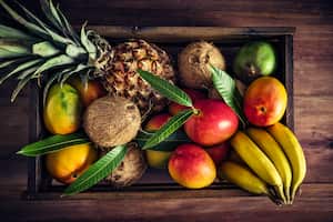 Wooden crates with assorted tropical fruits in rustic kitchen. Natural lighting. Mangos, pineapples, coconuts, bananas