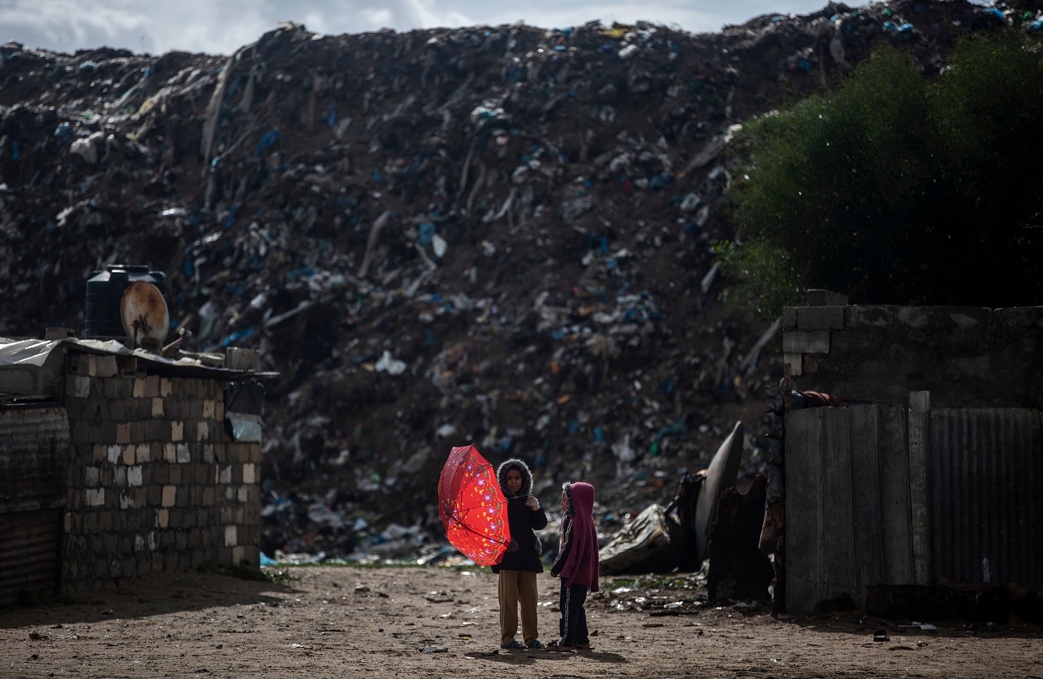 Dos niñas palestinas junto a montones de basura en un día lluvioso en un barrio pobre de Khan Younis, en el sur de la Franja de Gaza, el miércoles 20 de enero de 2021 (AP Photo / Khalil Hamra)