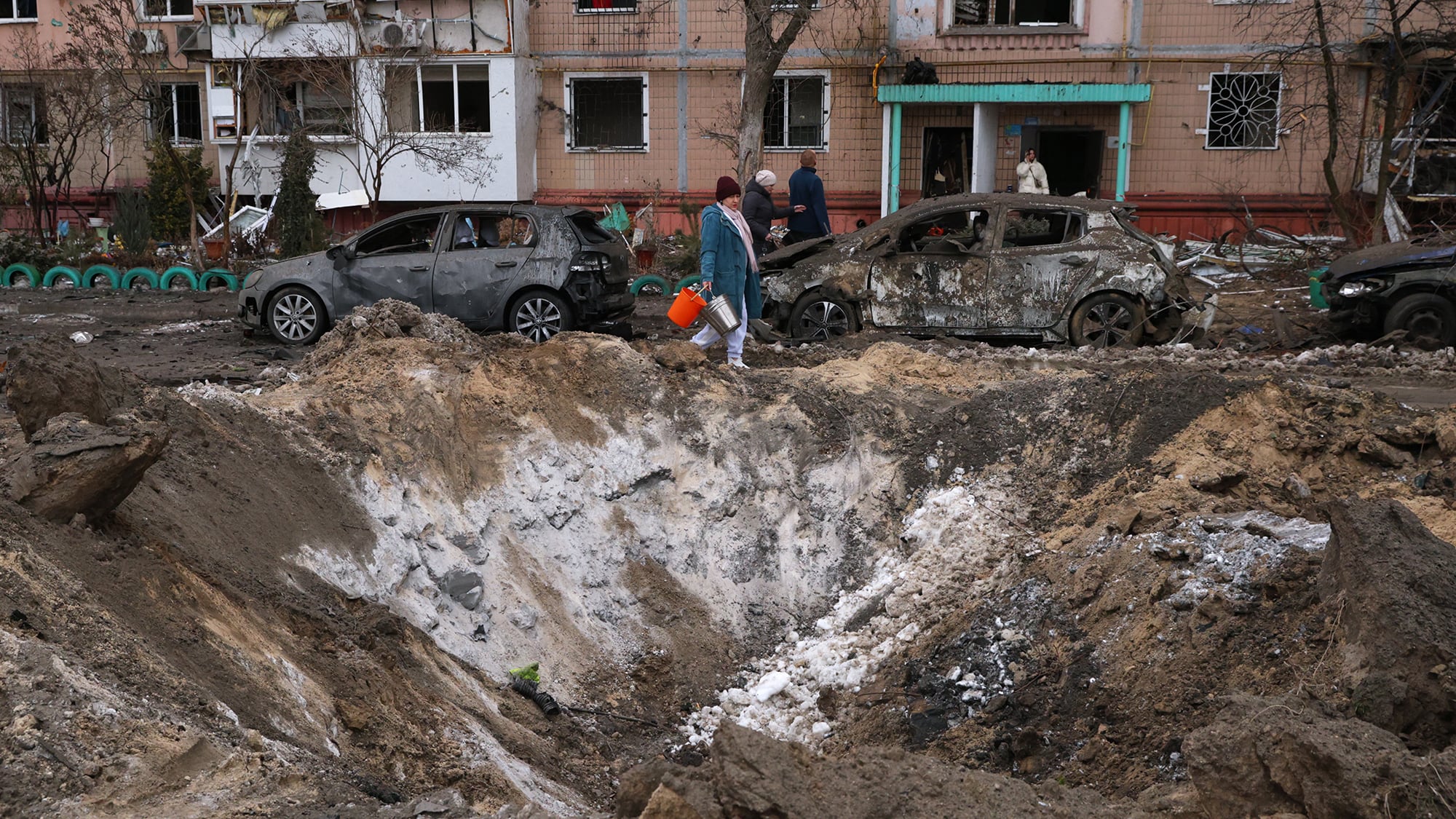 La gente pasa un cráter y daña coches cerca de un edificio de apartamentos después de un ataque ruso en Zaporizhzhia, Ucrania. Miércoles 28 de enero de 2026.