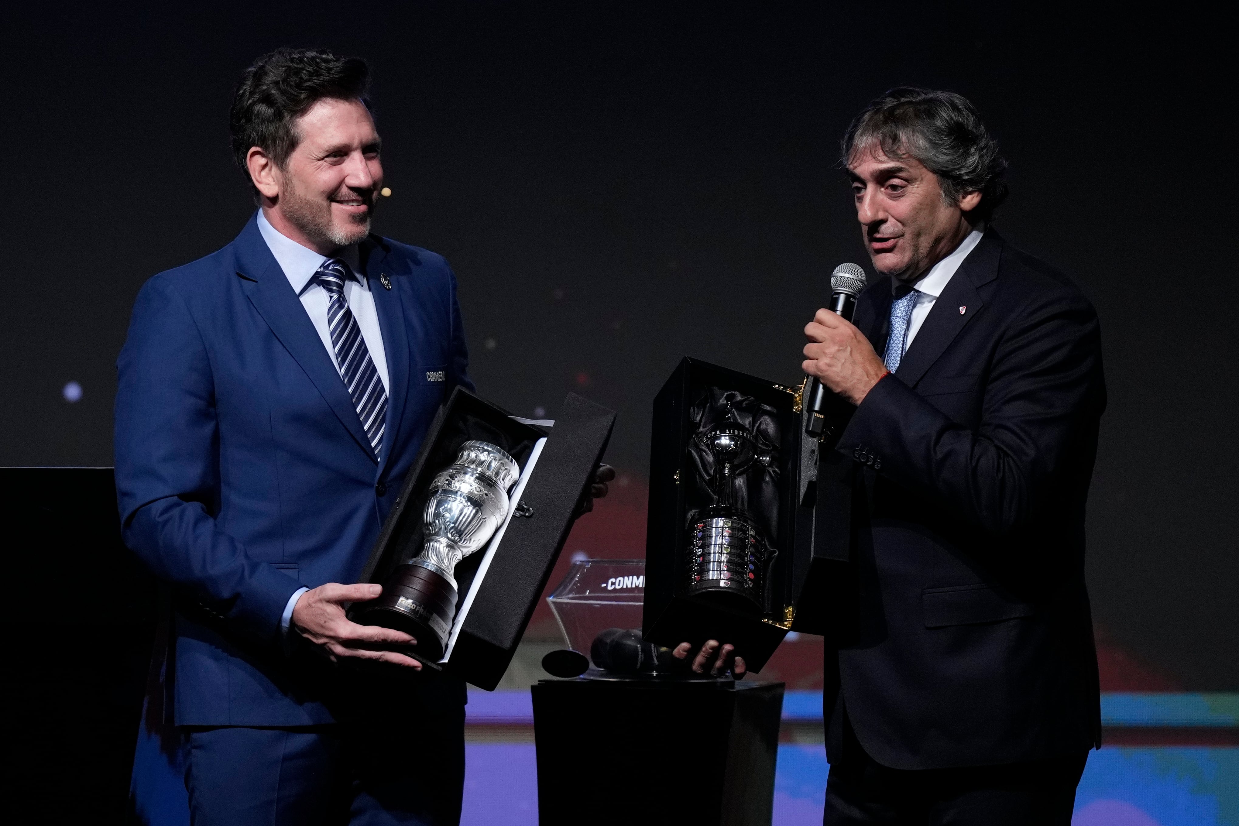 El presidente de la Conmebol, Alejandro Domínguez, izquierda, entrega réplicas de los trofeos de la Copa América y la Copa Libertadores al ex astro del fútbol uruguayo Enzo Francescoli durante la ceremonia del sorteo de la Copa Libertadores y Sudamericana en Luque, Paraguay, el lunes 18 de marzo de 2024. (Foto AP/Jorge Saenz)