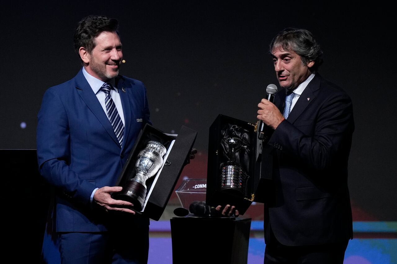 El presidente de la Conmebol, Alejandro Domínguez, izquierda, entrega réplicas de los trofeos de la Copa América y la Copa Libertadores al ex astro del fútbol uruguayo Enzo Francescoli durante la ceremonia del sorteo de la Copa Libertadores y Sudamericana en Luque, Paraguay, el lunes 18 de marzo de 2024. (Foto AP/Jorge Saenz)