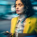 An Asian/Indian young adult businesswoman feels dizzy at night on a busy road because of the heavy use of a smartphone on the go.