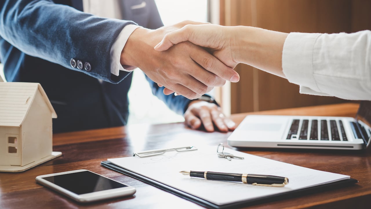 El agente inmobiliario y los clientes se dan la mano celebrando el contrato terminado después del seguro de vivienda y el préstamo de inversión, el apretón de manos y el trato exitoso.