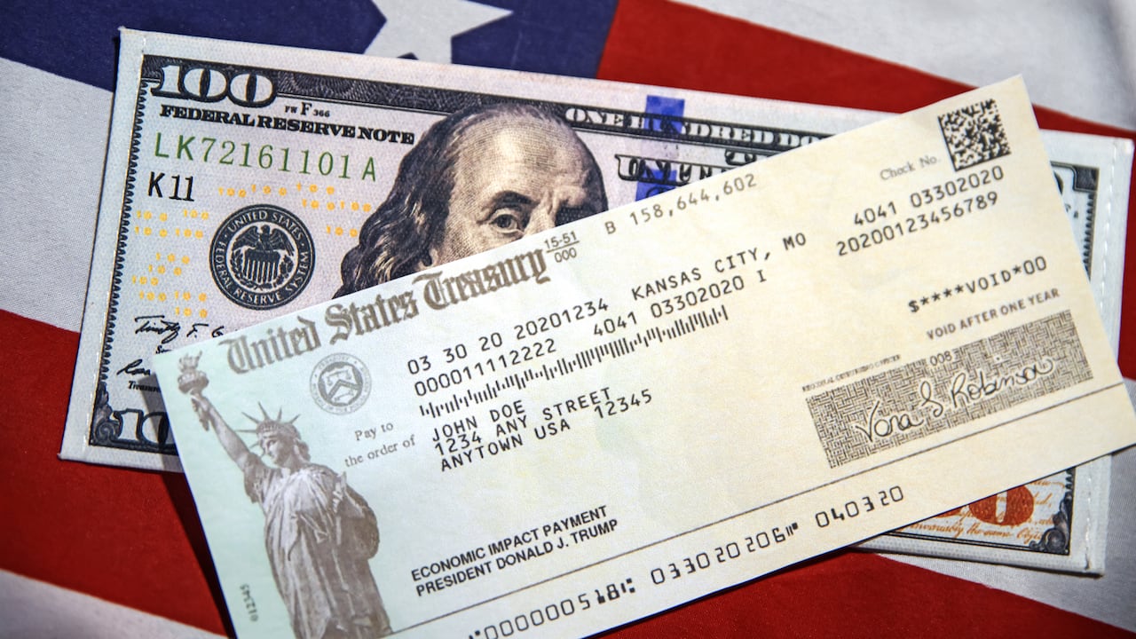 Cheque del Tesoro de Estados Unidos con billete de 100 dólares y bandera estadounidense de fondo.