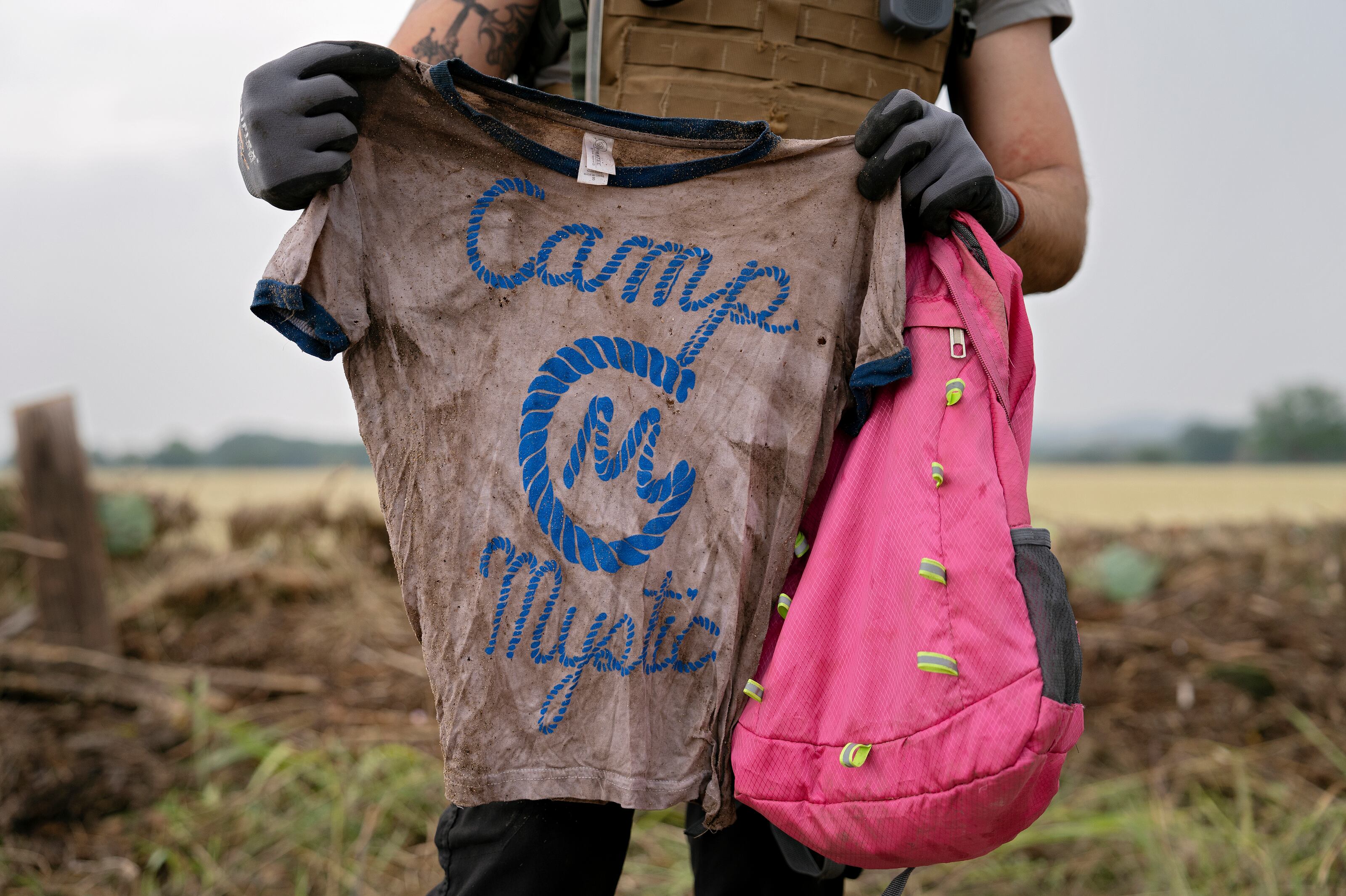 Un voluntario de búsqueda y rescate sostiene una camiseta y una mochila con las palabras "Camp Mystic" en Comfort, Texas.