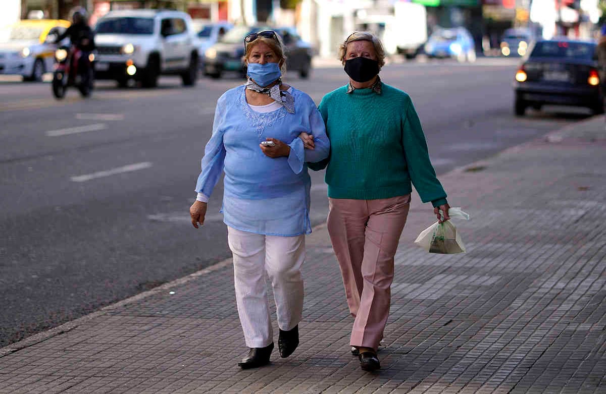 Las mujeres que usan mascarillas para prevenir la propagación del nuevo coronavirus caminan de la mano en una calle de Montevideo, Uruguay. (Foto AP / Matilde Campodonico)