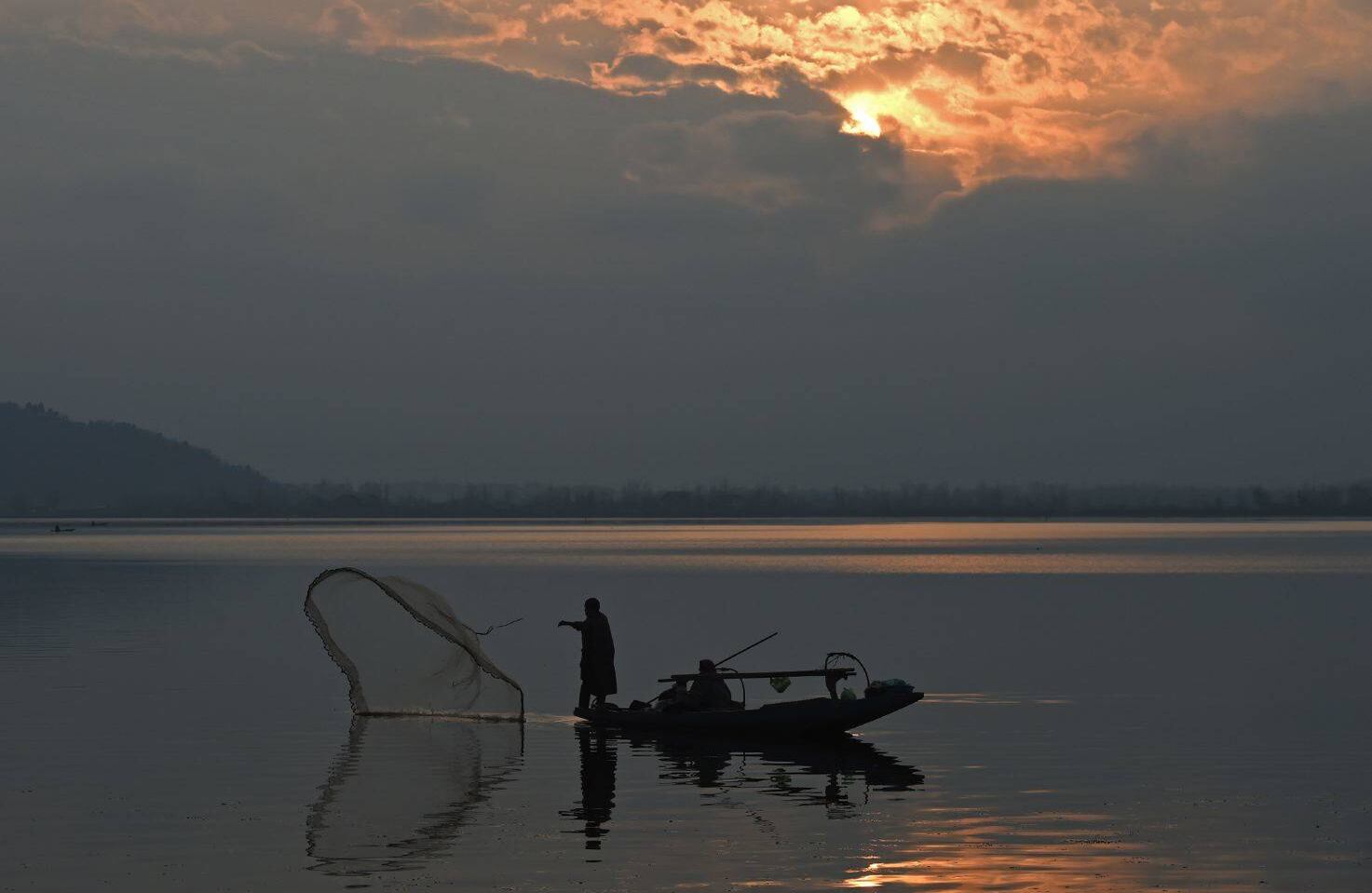 Un pescador de #cachemira #India arroja su red desde su bote durante el #atardecer en el lago Dal en Srinagar el 30 de enero de 2018. / AFP PHOTO / TAUSEEF MUSTAFA 