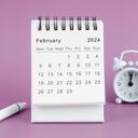 Desk Calendar 2024: February calendar is used to plan daily work and life with alarm clock and white pen against a pink background.