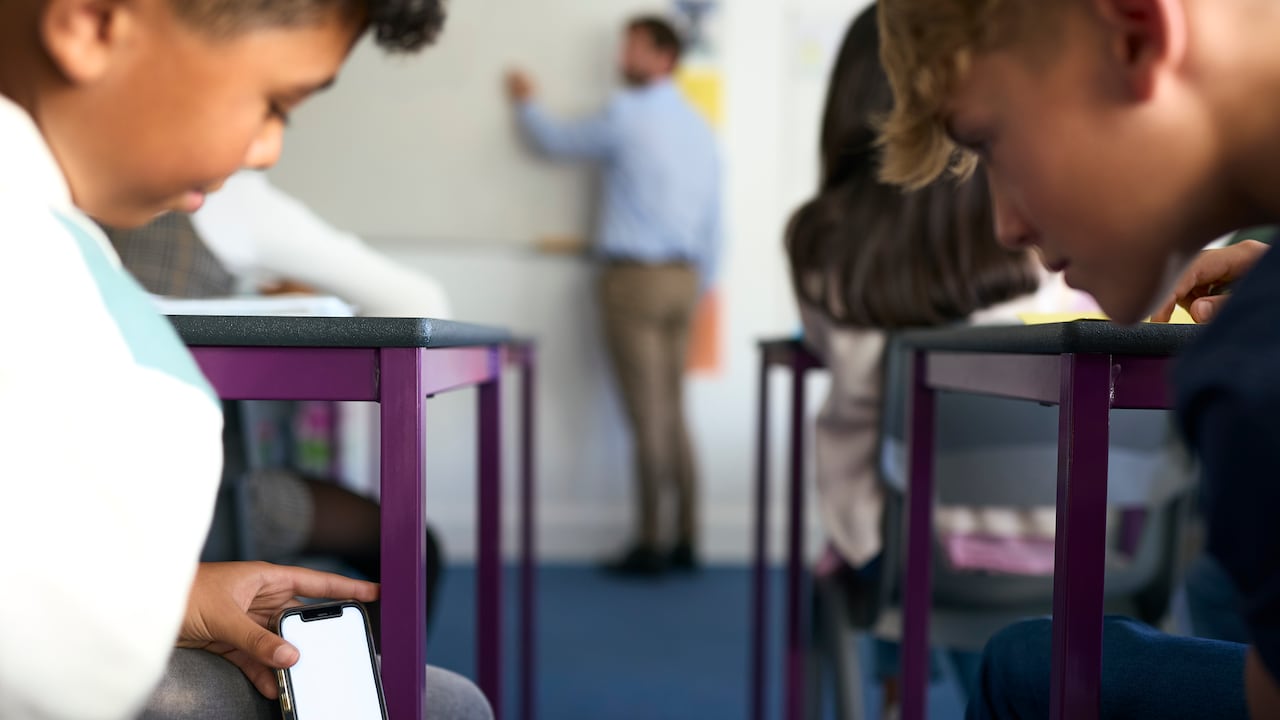 Jovenes revisan su celular en una aula de clase. Imagen de referencia