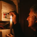 A senior man investigates his fuse box at home - by the light of a candle only - in a blackout during the energy crisis.