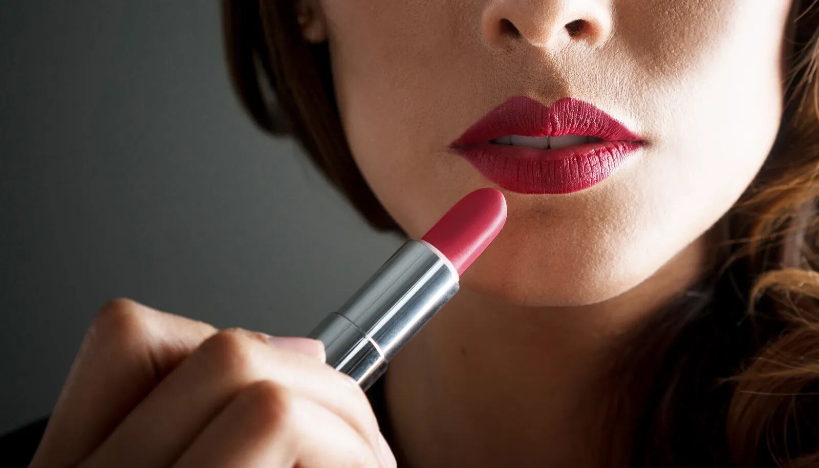 Close-up on a woman applying red lipstick on her lips straight from the bullet - makeup concepts