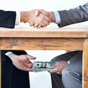 Cropped shot of two businessmen shaking hands while money passes hands under a table