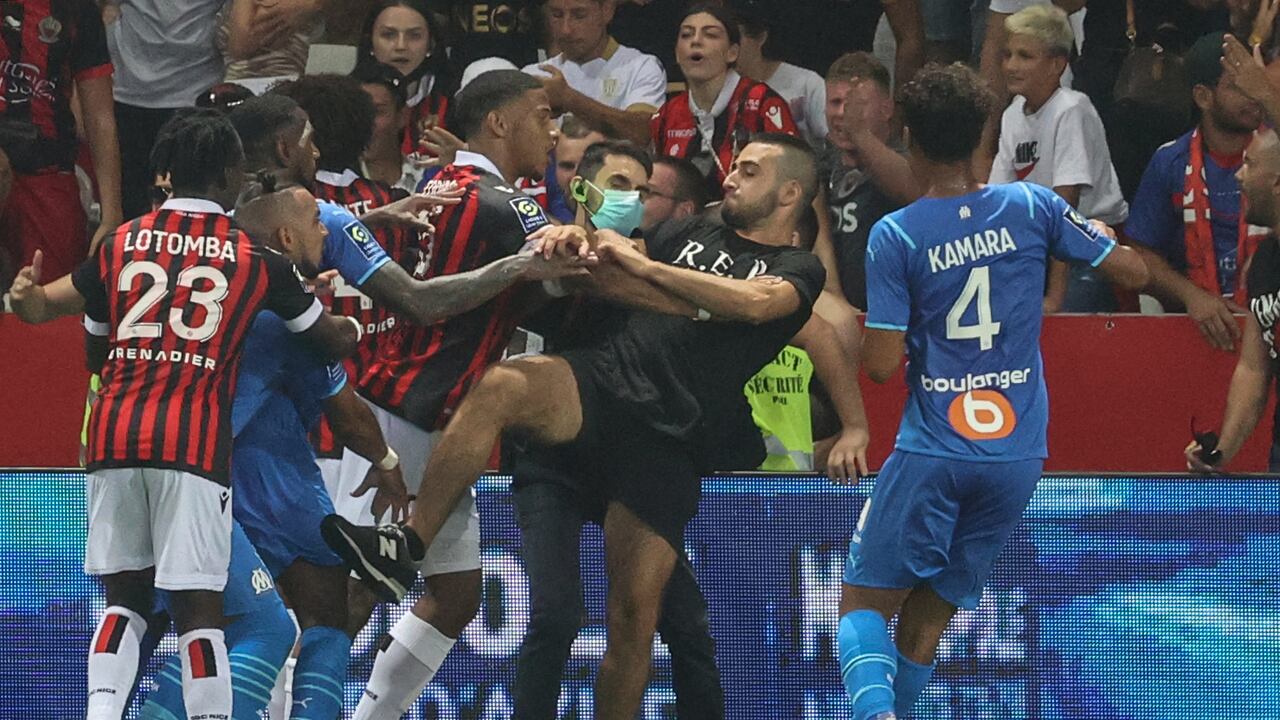El mediocampista francés del Marsella, Dimitri Payet (2L) reacciona cuando los jugadores de OGC Nice (camiseta roja y negra) y Olympique de Marseille (camiseta azul) detienen a un fan que invade el terreno de juego tratando de patear a Payet durante el partido de fútbol francés L1 entre OGC Nice y Olympique. de Marseille (OM) en el estadio Allianz Riviera en Niza, sur de Francia, el 22 de agosto de 2021. - El partido de la Ligue 1 francesa entre Niza y Marsella se detuvo el 22 de agosto de 2021, cuando los fanáticos del equipo local invadieron el terreno de juego y enojados se enfrentó al jugador contrario Dimitri Payet. Un periodista de la AFP en el partido dijo que los problemas estallaron en el minuto 75 cuando la estrella del Marsella Payet, quien había sido atacado con botellas de plástico cada vez que tomaba una esquina, lanzó una de regreso a las gradas. (Foto de Valery HACHE / AFP)