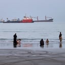 Gente pasa tiempo en la playa mientras se ven mercantes fondeados detrás en el estrecho de Ormuz, cerca de Bandar Abbas, Irán.