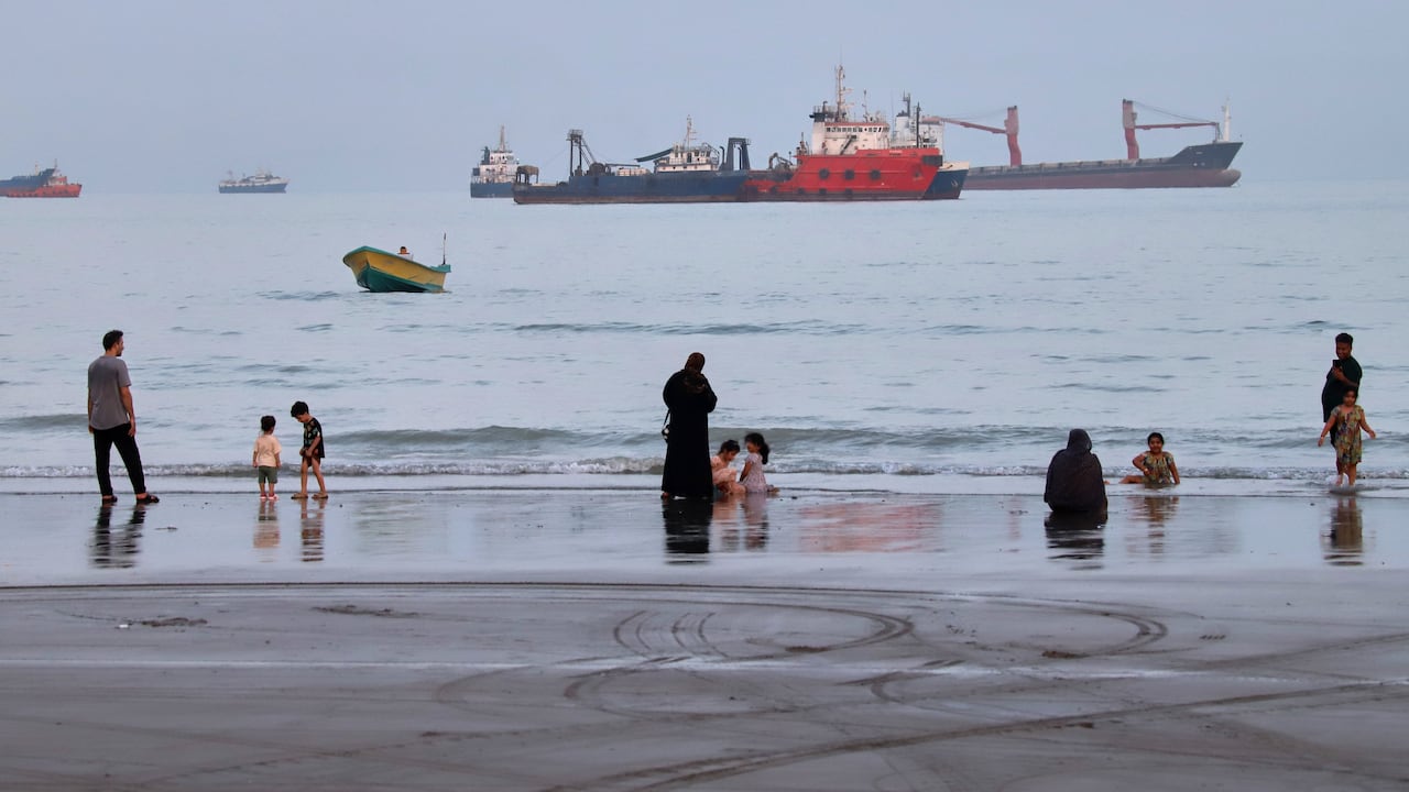 Gente pasa tiempo en la playa mientras se ven mercantes fondeados detrás en el estrecho de Ormuz, cerca de Bandar Abbas, Irán.