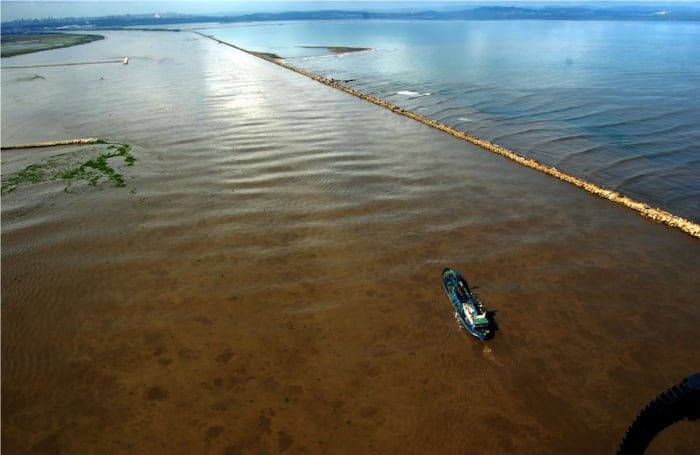 Barco mercante ingresa al río Magdalena en la desembocadura en Bocas de Ceniza a la altura del Dique Direccional o Tajamar. Al fondo Barranquilla y a la derecha el mar Caribe.