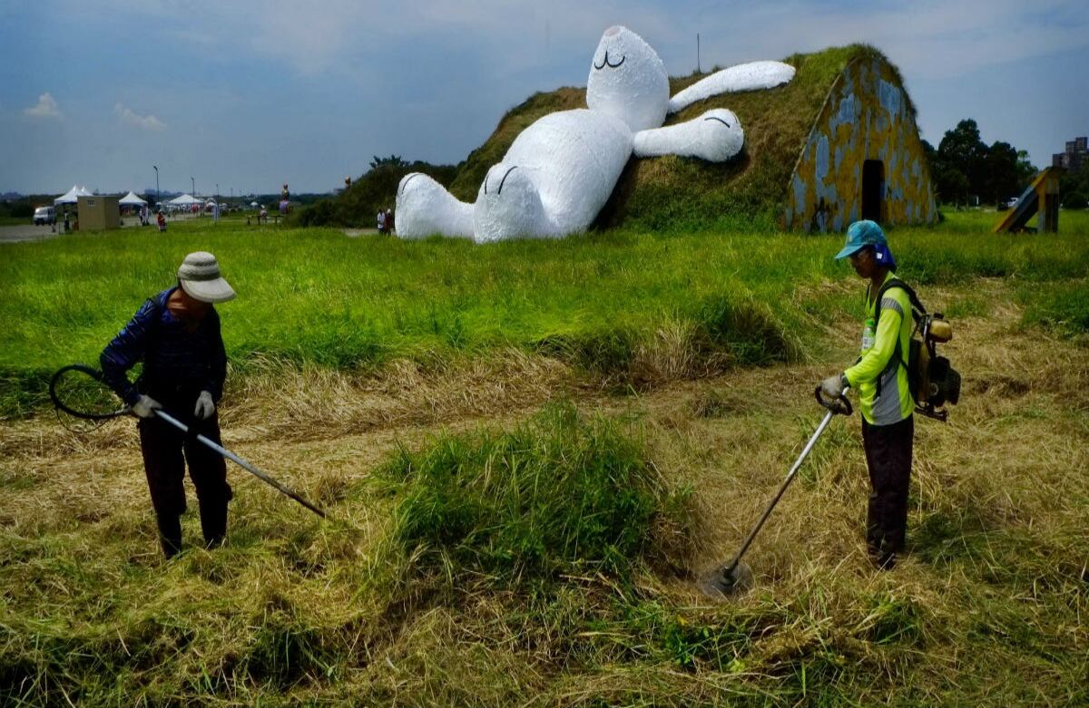 Paisajistas podan el césped en frente de una obra del artista Florentijn Hofman, un conejo blanco de 25 metros de altura. La obra se presentará en Taiwan. (AP)