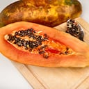 A papaya sliced in half on a cutting board. Its seeds are half spooned