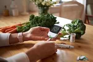 Young woman measuring her blood sugar using glucometer sitting at the table in living room.