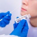 Médico con guantes protectores y ropa de trabajo con un kit de prueba para la prueba de coronavirus. El médico está recolectando una muestra nasal para una joven con un hisopo de muestreo. Covid