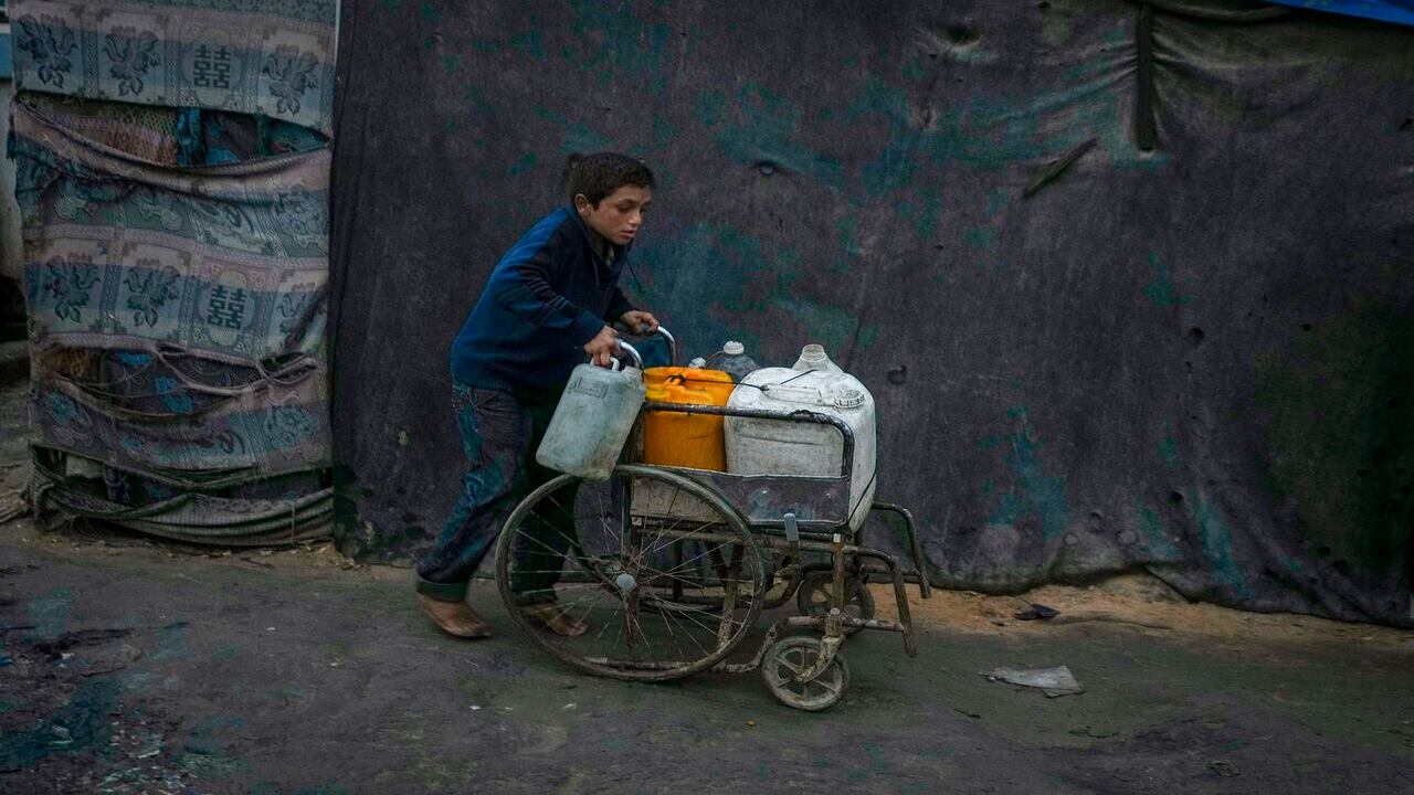 Un niño palestino empuja una silla de ruedas que transporta bidones y botellas de plástico con agua en un campamento para desplazados, en Deir al-Balah, Franja de Gaza