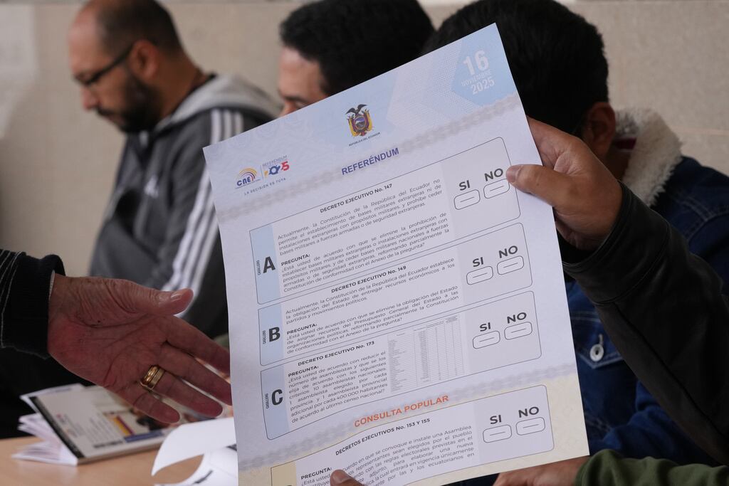 Una funcionaria electoral entrega una papeleta a un votante en un referendo sobre si permitir bases militares extranjeras en el país y reescribir la constitución a través de una asamblea constituyente, en Quito, Ecuador.