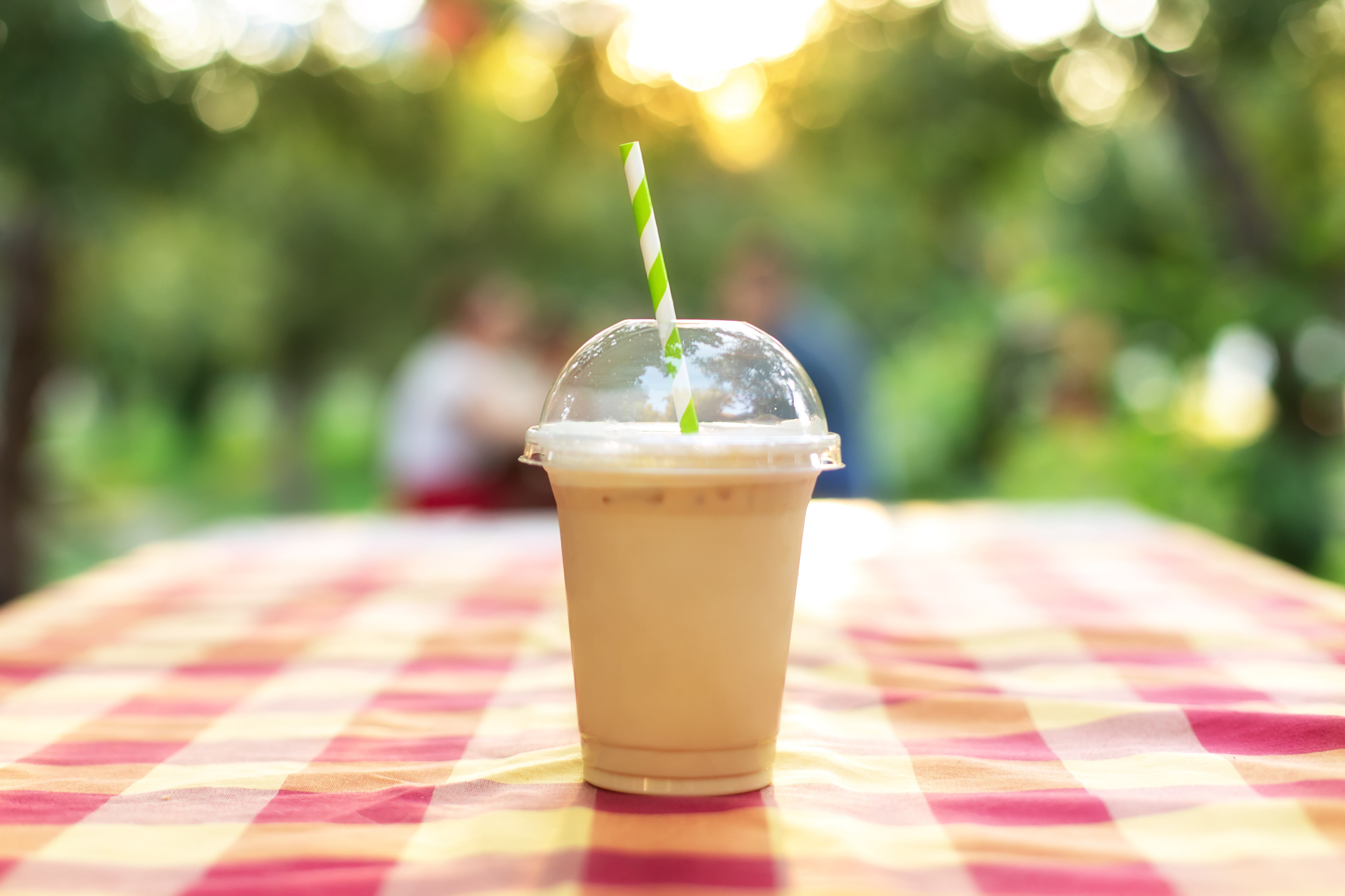 Cold iced coffee with milk on table in green background. Ice coffee in a tall glass with cream poured over and coffee beans. Cold summer drink in garden. Caramel frappe coffe in Street coffee shop