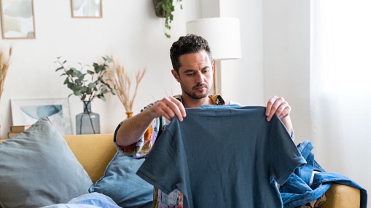 Man sorting and folding his clothes while sitting on a sofa in the living room at home.