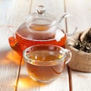 Taza de té, tetera y hojas de té en la mesa de madera