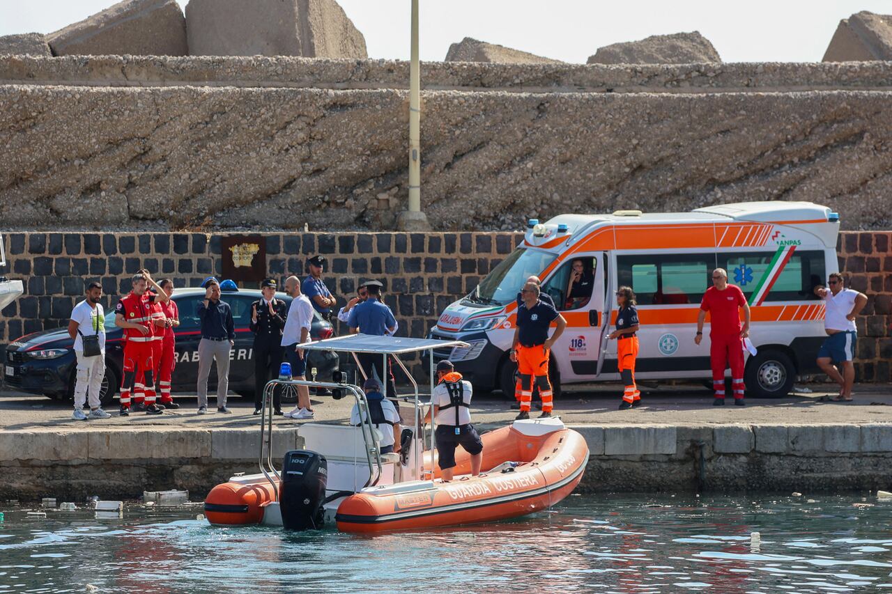 Los carabineros italianos se encuentran en el muelle con trabajadores de la salud observando un barco de la Guardia Costera que se prepara para buscar a otras seis personas desaparecidas después de recuperar a una víctima debido al hundimiento de un velero frente a la costa de Porticello, al noroeste de la isla de Sicilia, el 19 de agosto de 2024. (Foto de Igor Petyx / ANSA / AFP)